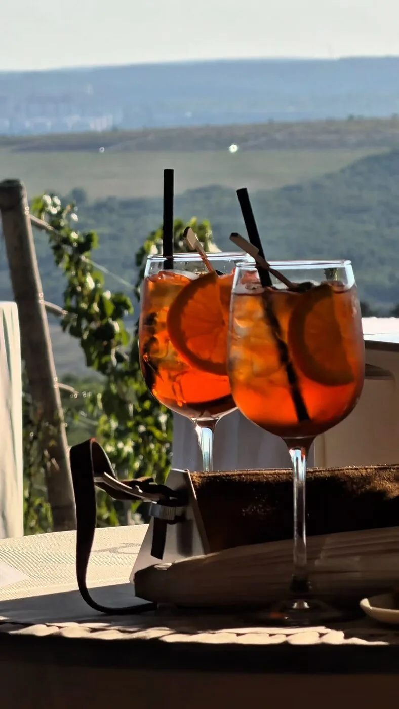 Cocktailuri servite cu felie de portocală, pe fundal de podgorie